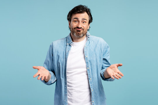 Confused man shrugging shoulders gesturing i don't know on blue background