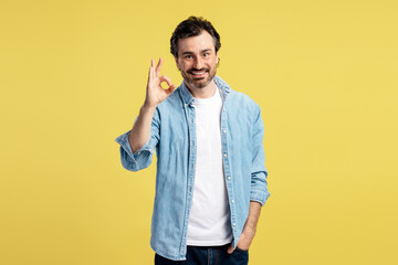 Smiling man showing ok sign on yellow background