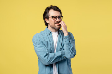 Pensive entrepreneur biting nails and feeling anxious on yellow background