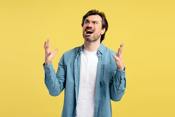 Frustrated man screaming and gesturing on yellow background