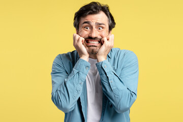 Scared man clutching face in fear on yellow background