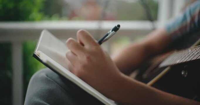 Young male musician sitting on a porch, playing guitar and writing a song