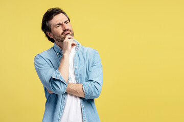 Pensive man touching chin and looking away on yellow background