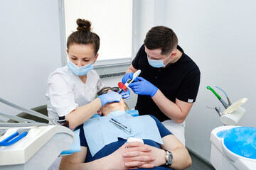 Dental Curing Light: Polymerization Process. Dentist and assistant applying filling to patient's tooth in modern dental clinic. Teamwork in Dentistry.