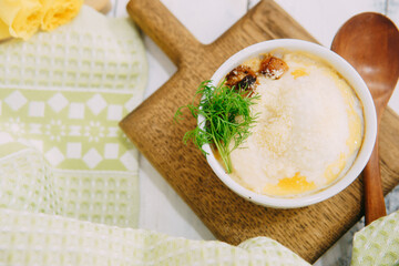 Baked casserole served in a white ramekin garnished with fresh green dill on a wooden board, accompanied by yellow roses and soft light.