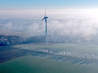 Aerial view of a wind turbine in a winter landscape with sun and deep fog over the fields, wind...