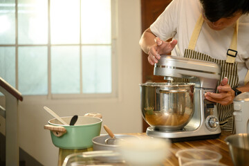 Young asian man operating a stand mixer to whip cream in a cozy kitchen