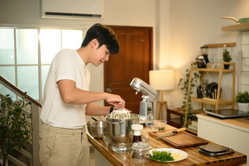 Young asian man operating a stand mixer to whip cream in a cozy kitchen