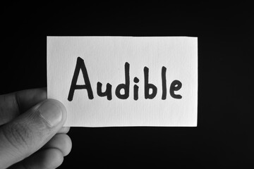 Hand holding a paper card with the word AUDIBLE