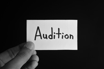 Hand holding a paper card with the word AUDITION