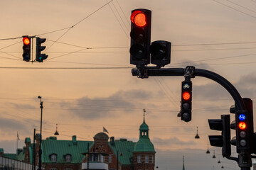 Traffic lights in city intersection during sunset in Copenhagen, silhouetted urban infrastructure with warm tones and historic rooftops in the distance.