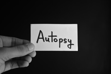 Hand holding a paper card with the word AUTOPSY