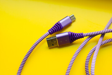 Close-up of two connectors of a purple and white braided USB cable on a bright yellow background....
