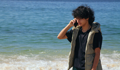 young Hispanic Latino man walking along the shore talking on the phone
