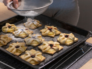 A woman dusts a pineapple wedge and cherry wrapped in a puff pastry with powdered sugar. Baking