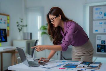 Fototapeta premium Young professional woman analyzing financial charts and working with data on a laptop in a modern office, focused on business strategy and growth