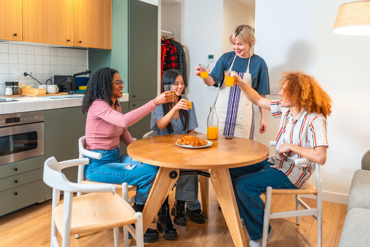 Roommates toasting orange juice at kitchen table