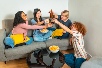 Friends toasting drinks at home party, sitting on sofa and floor