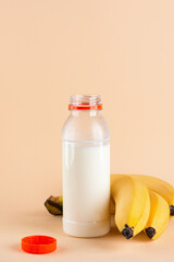 Fresh banana milk drink in a bottle with bananas on a beige background. Traditional Korean drink. Vertical orientation.