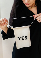 A woman in a black blouse holds a small banner that says 'YES', signifying agreement or affirmation