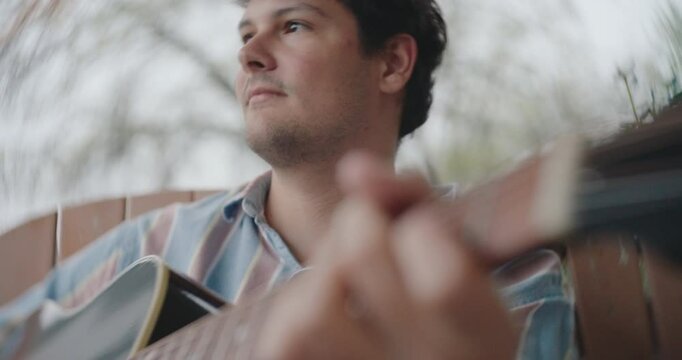 Young male musician sitting on a porch, playing guitar and writing a song