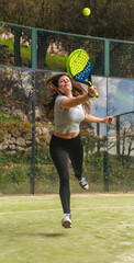 A young and strong athlete playing padel, jumping to hit the ball with a racket and looking very...