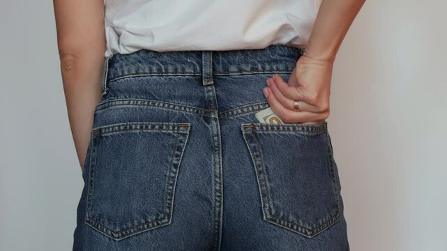 A close-up of a girl carefully tucking dolars into her pocket, a symbol of savings and reasonable consumption.