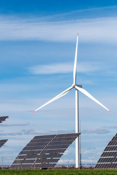Wind turbine with solar panels in foreground. Renewable energy infrastructure in Zaragoza, combining wind and solar sources in clear sky and rural context.