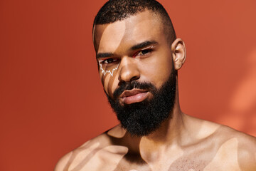 Obraz premium Stylish young man exuding confidence under playful sunlight patterns in a vibrant orange backdrop