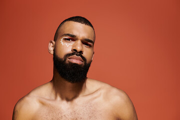 Stylish man with artistic facial paint poses confidently in front of an orange backdrop