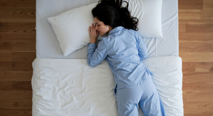 Woman in blue pajamas sleeping on white bed with wooden floor. Sleep quality concept for mattress advertising and insomnia treatment products