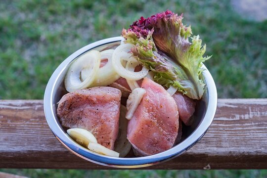 Pork balyk sliced and prepared for barbecue. Marinated meat with onions and herbs in a metal bowl.