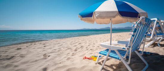Blue and white beach umbrella is on the sand. There are two chairs under the umbrella