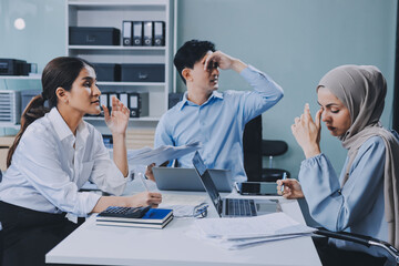 Young asian businesswoman suffering from headache while colleagues arguing and blaming her for bad work results during stressful office meeting