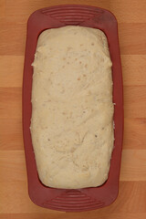 Unbaked bread dough sits in a maroon silicone loaf pan on a wooden surface