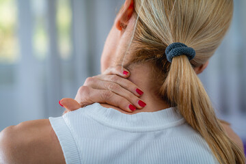 Naklejka premium Woman experiencing neck pain, holding her sore neck with discomfort. The image highlights muscle strain, stiffness, or possible injury due to stress, poor posture, or prolonged screen use.