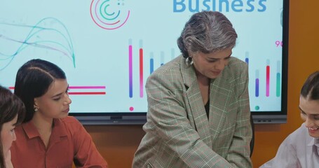 Indian asian young female old senior boss lady team leader show chart board learn study graph data growth work place adult girl talk speak share stock trade idea plan staff group job office day - Powered by Adobe