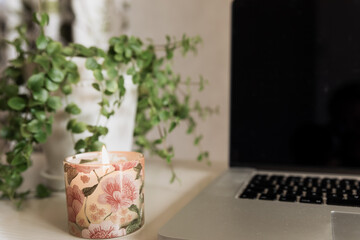 Cozy workspace detail with floral candle, greenery and laptop