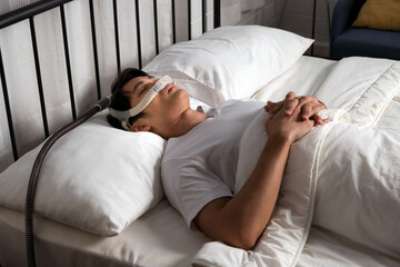 Asian man sleeping calmly with CPAP nasal mask in bed, a treatment for snoring and obstructive...