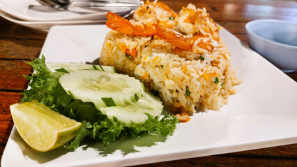 Shrimp fried rice served on white plate garnished with sliced cucumbers, lettuce, and a lime wedge