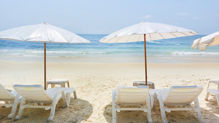 Beach chairs and umbrellas standing on a tropical beach invite tourists to enjoy summer vacations