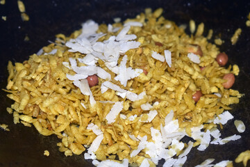 A bowl filled with crispy snacks topped with shredded coconut and peanuts sits in a rustic kitchen environment, showcasing delightful flavors