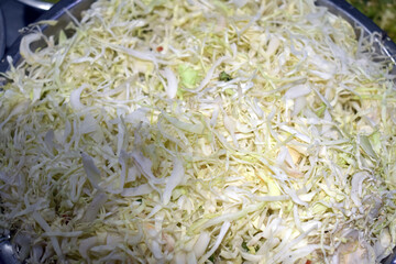 Large mound of finely shredded cabbage sits in a stainless steel bowl in a well-lit kitchen, ready for cooking or salad preparation