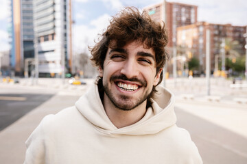Portrait of young happy man smiling at camera standing at city street. Youth and people concept