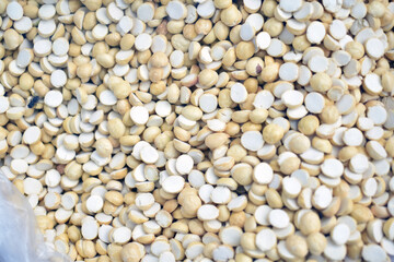 Many small dried seeds are spread out on a surface in a market, showcasing their beige and white colors in natural light