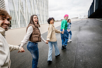 Diverse group of young friends running happily together while holding hands. Youth community,...