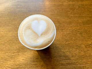 Coffee latte art on wood table in cafe nature light close-up. Сappuccino with a pattern in a paper cup on a wooden table in a coffee shop top view. The concept of food and drinks.