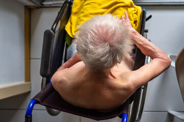 Old nude lady with white hair, in a wheelchair,