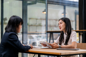 Two women are sitting at a table, one of them holding a piece of paper