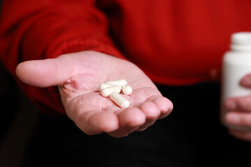 Close-Up Of Several White Capsules Held In The Palm Of A Wrinkled Hand, With A Blurred Bottle In...